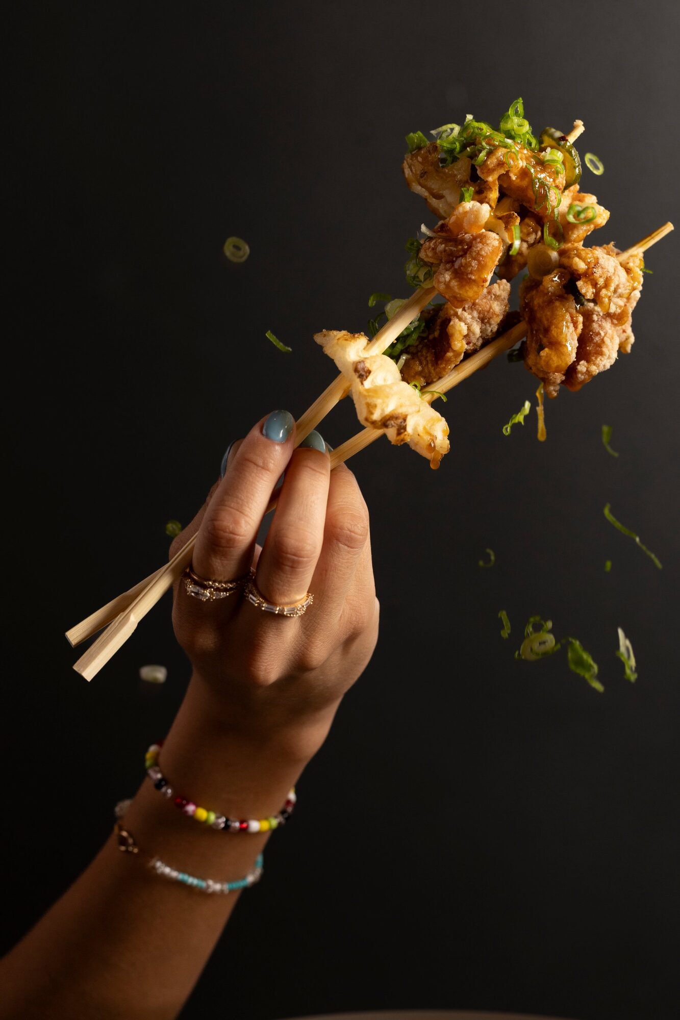 Glazed karaage held high in chopsticks with scallions falling