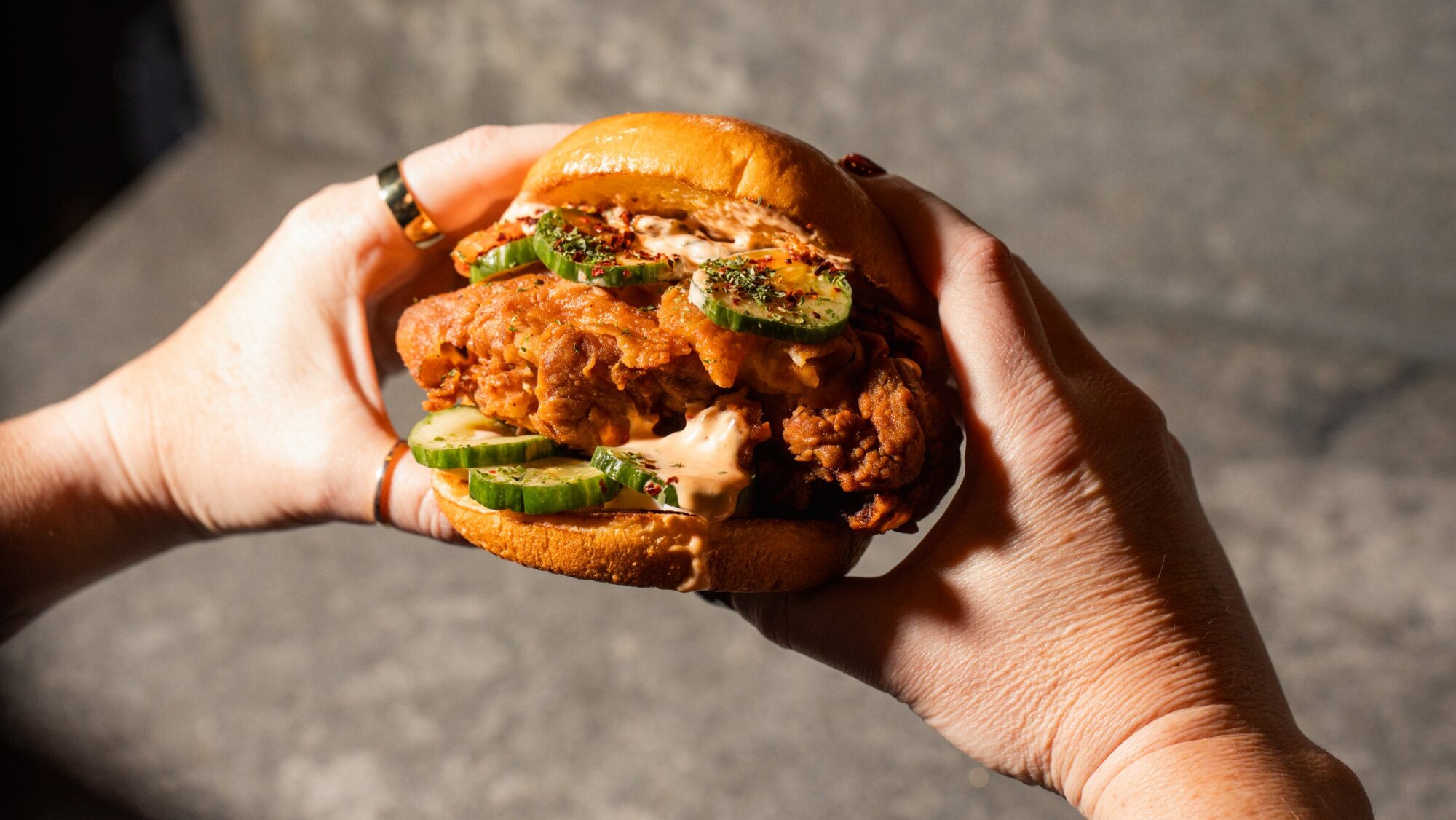 Crispy chicken sandwich with cucumbers held in two hands