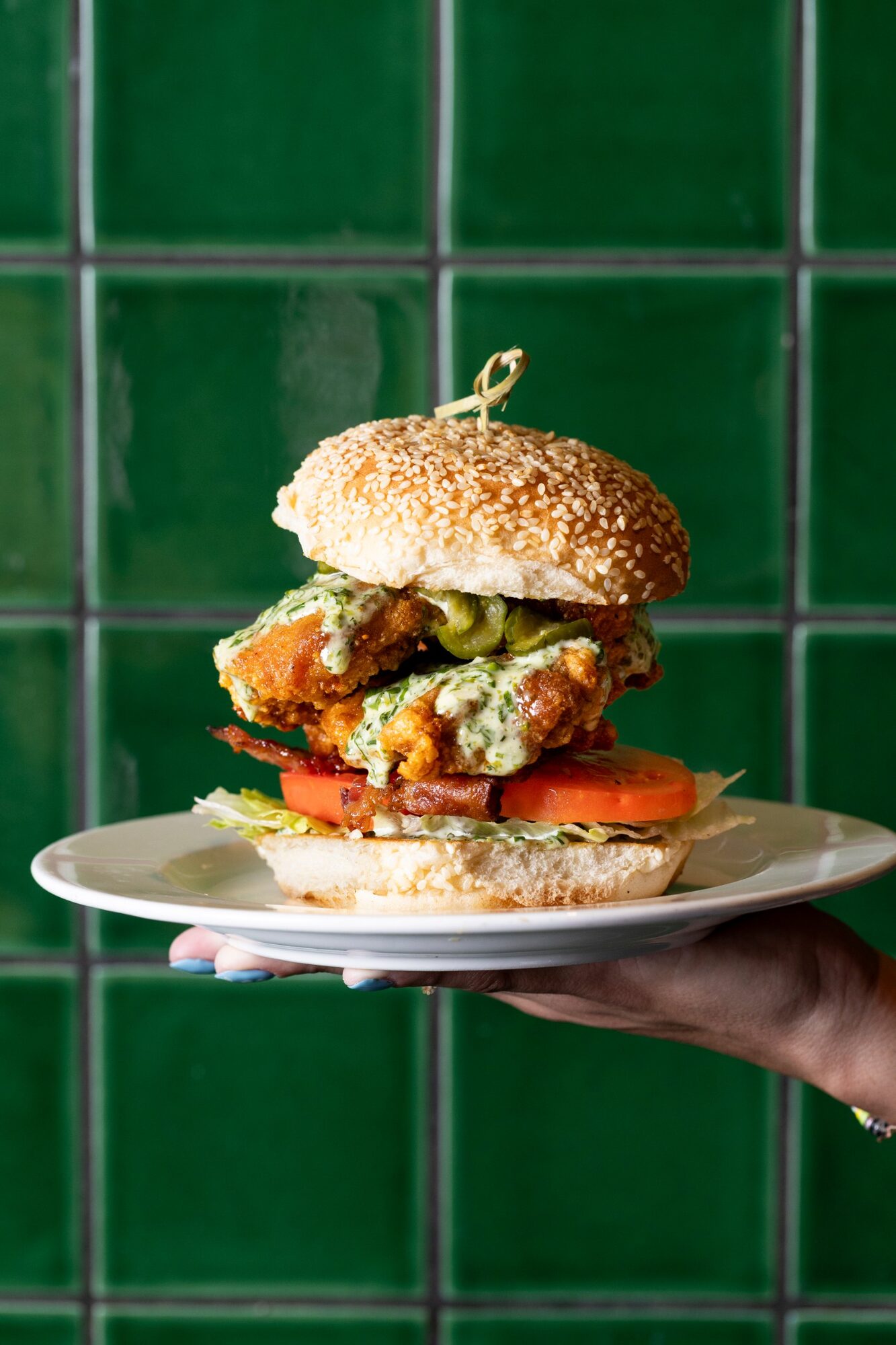Crispy chicken sandwich with bacon and tomato against green tile