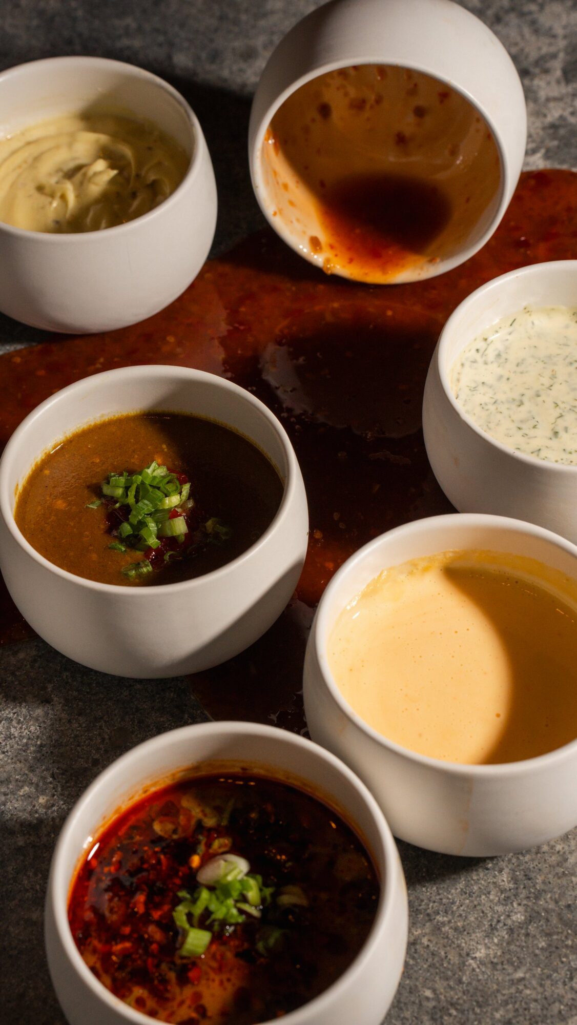 Six Clucks sauces in white cups over a spill of chili glaze