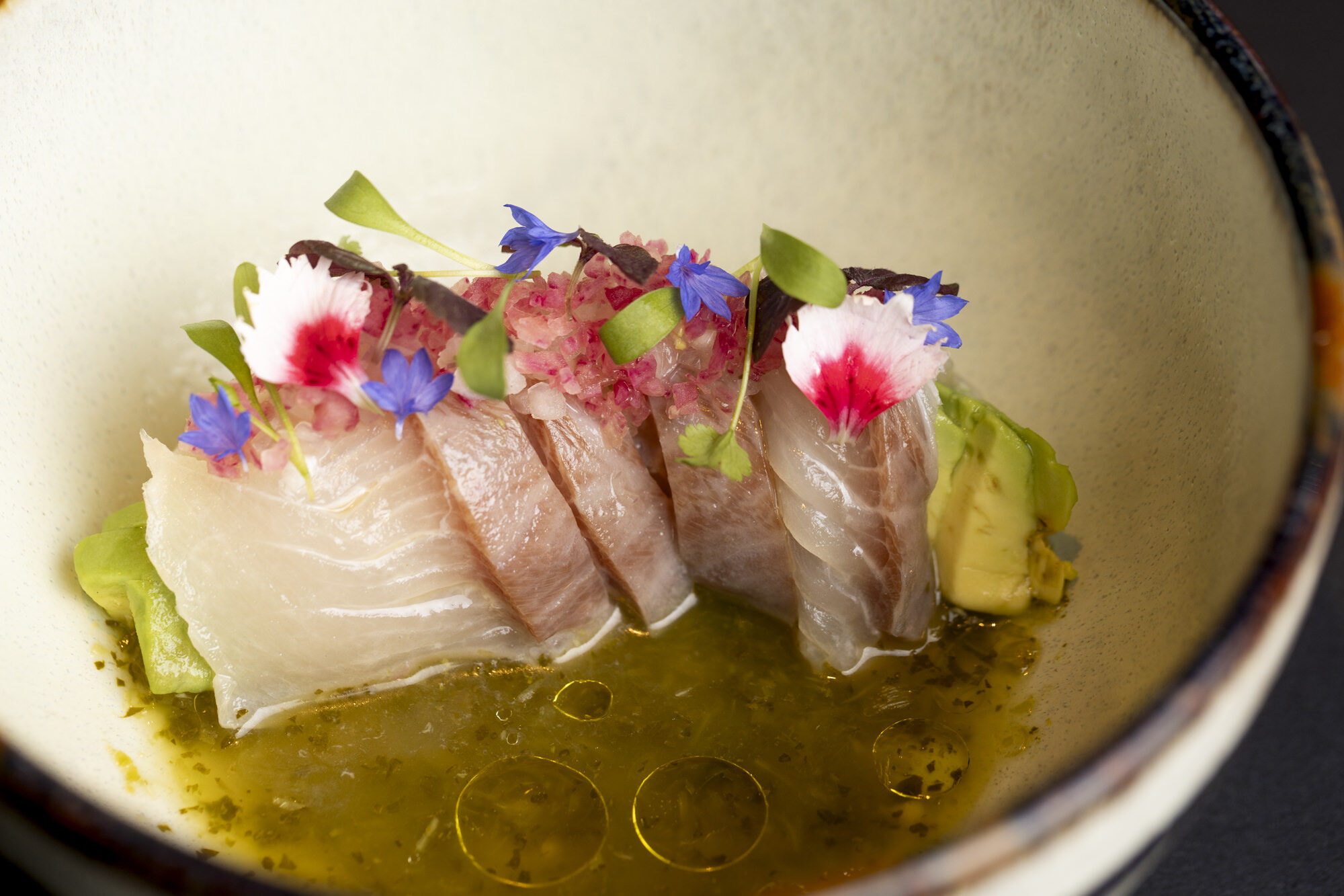 Hamachi crudo with flowers in a ceramic bowl